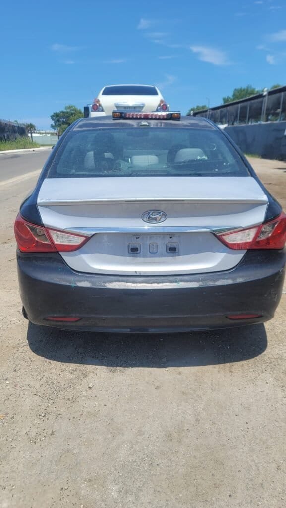 Hand holding cash in front of a junk car being towed in Miami-Dade County, emphasizing quick payment for unwanted vehicles.
